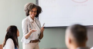 Businesswoman gestures during a presentation in front of a group of attentive colleagues.