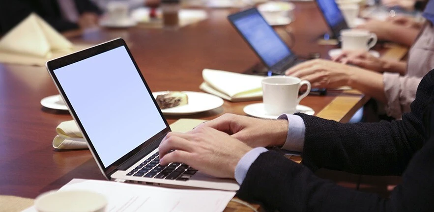 Employees using computer laptops during conference meeting around a table.
