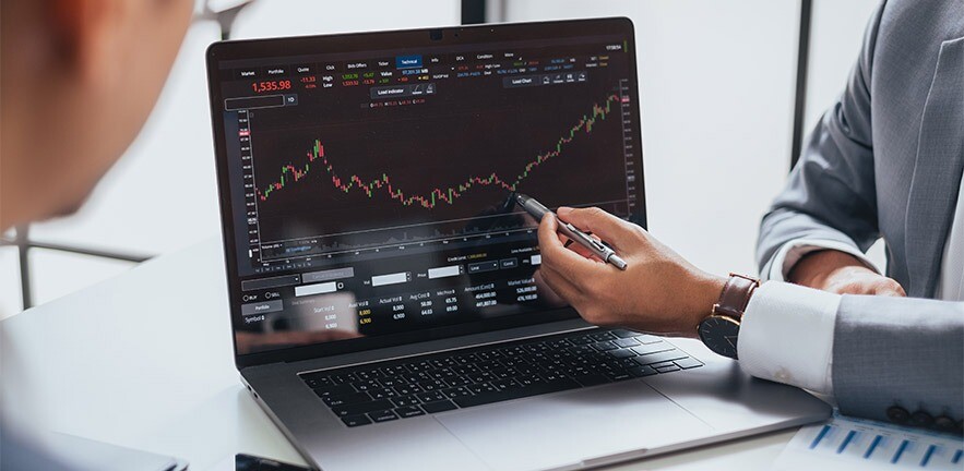Businessmen talking about investments and finance pointing at a graph on a laptop.