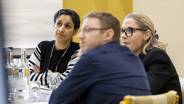 Two women and a man listening in a classroom setting.