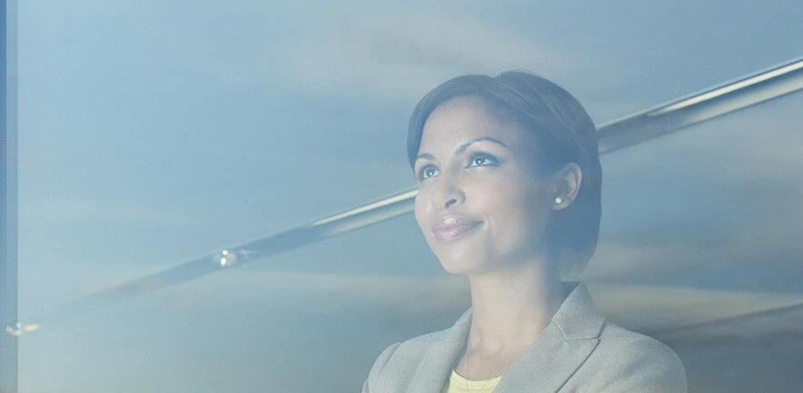 Suited woman gazes out of the window up towards the sky, deep in thought.