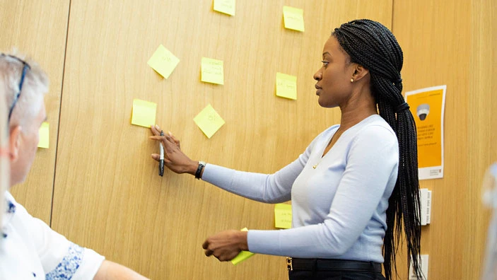 A participant places sticky notes on a wooden wall during an Executive Education workshop.