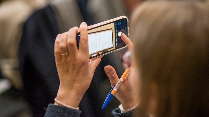 An EnterpriseWOMEN participant using a smartphone to photograph a presentation.