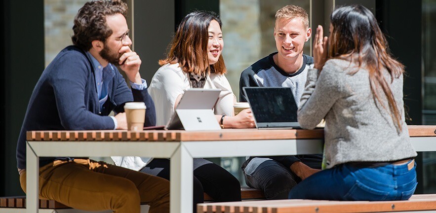 Cambridge MBA students sitting at a table in one of the outdoor spaces at the Business School