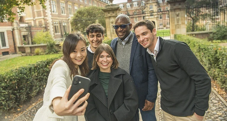 MFin students take a group selfie in front of a Cambridge College.
