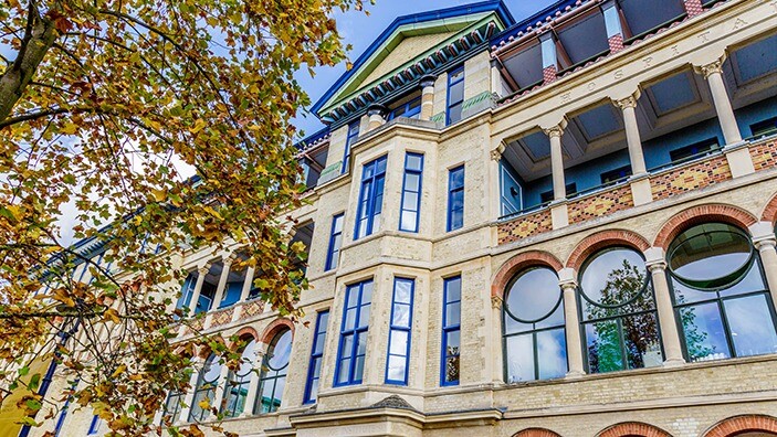 Cambridge Judge Business School in the autumn, surrounded by yellow-leaved trees.