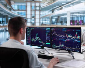 Man sitting at his desk looking at graphs and data on a computer.