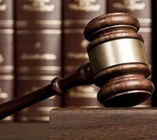 A wooden gavel rests on a table, with law books blurred in the background.