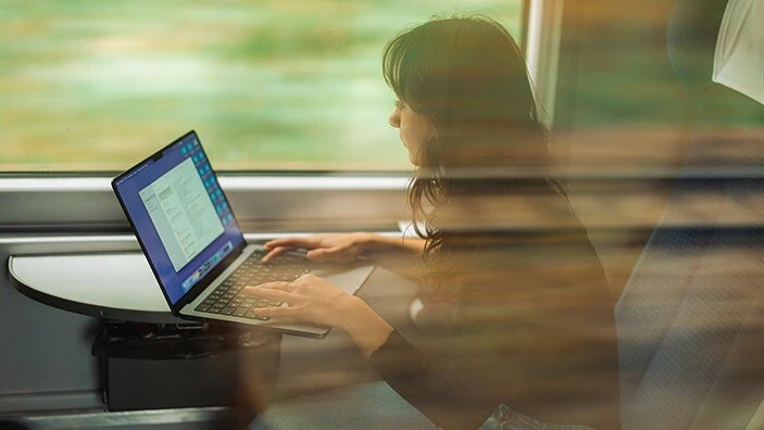A woman uses a laptop while sitting on a train.