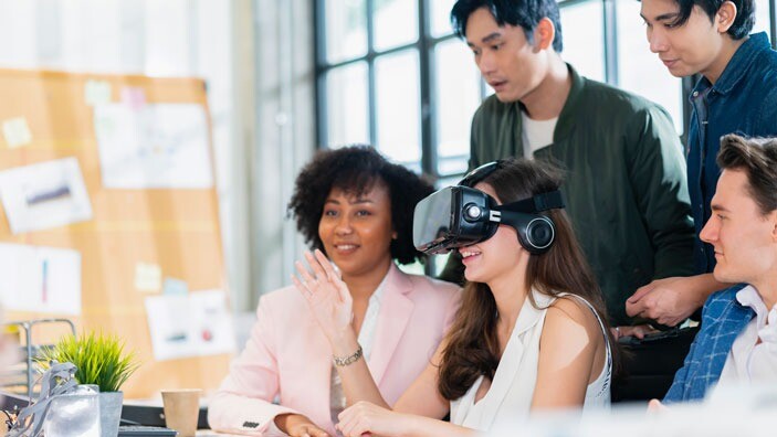 A group of colleagues observe a woman using virtual reality technology, engaging in creative collaboration.