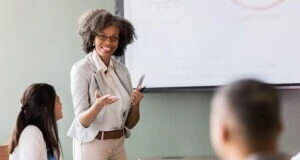 Businesswoman gestures during a presentation in front of a group of attentive colleagues.