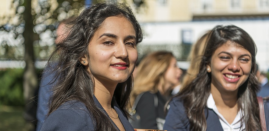 Female MBA students in a crowd of their classmates enjoying discussion in front of the campus.