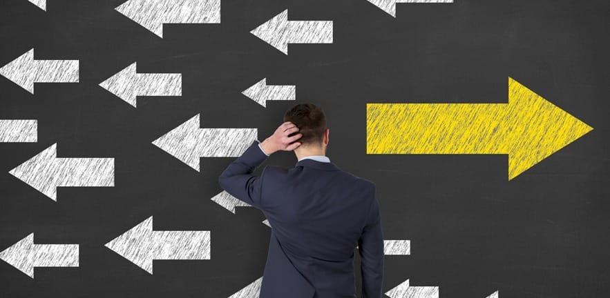 A confused man scratches his head while looking at arrows in a blackboard all going in different directions.