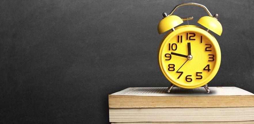 A bright yellom alarm clock rests on a stack of books.