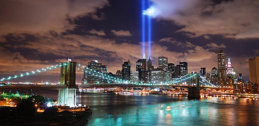 New York City Manhattan panorama view with Brooklyn Bridge at night with office building skyscrapers skyline illuminated over Hudson River and two light beam in memory of September 11.