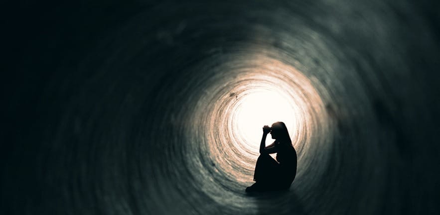 The silhouette of a woman sitting in a dark tunnel with a light at the end.