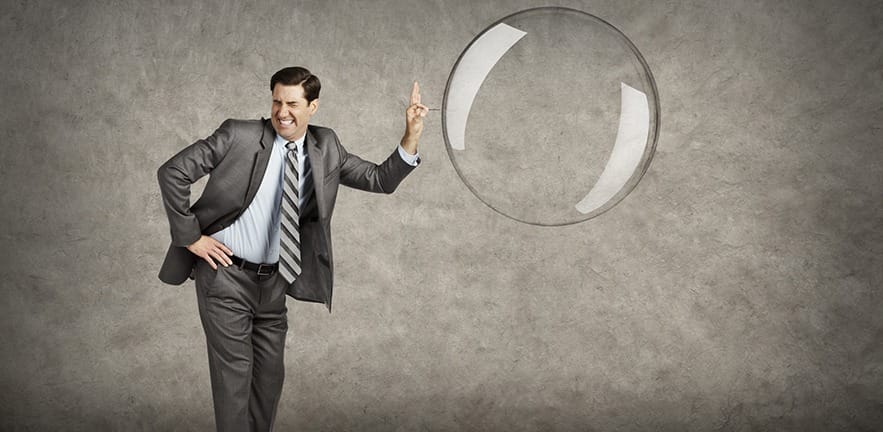 A businessman about to pop a large bubble with a pin.