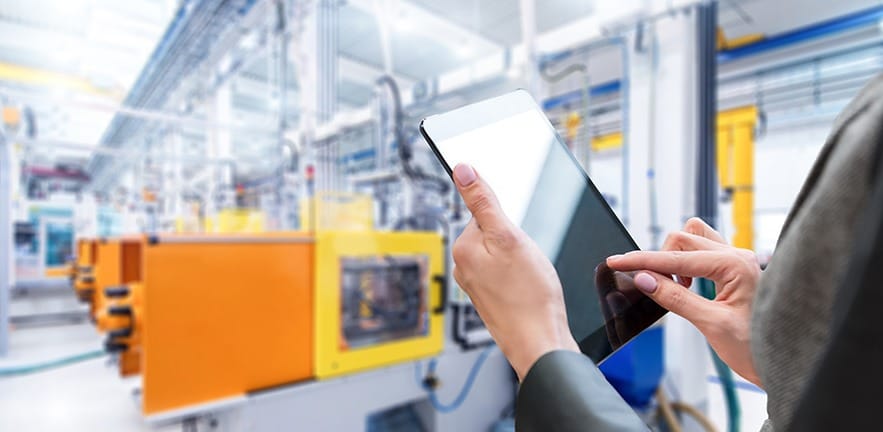 Horizontal color image of businesswoman - unrecognizable person - working with digital tablet in large futuristic factory. Focus on businesswoman's hands holding black tablet, futuristic machines in background.