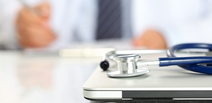 Medical stethoscope lie on closed PC closeup while doctor works in background.