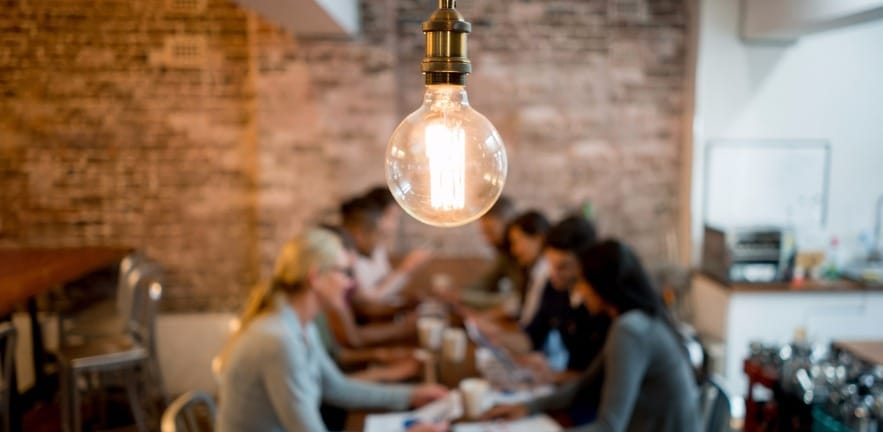 Small business jumpstart - glowing lightbulb with office workers in background