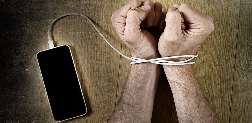 man hands trapped and wrapped on wrists with mobile phone cable as handcuffs in smart phone networking and communication technology addiction concept