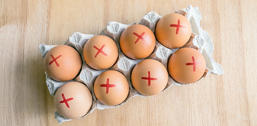 Top view of brown farm eggs with red cross in white carton indicating recalled product.