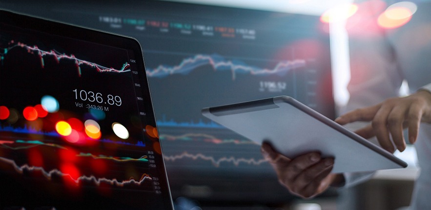 Businessman using tablet and laptop for analysing stock market data.