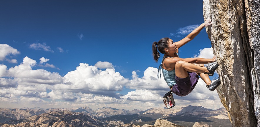 Female climber dangles from the edge of a challenging cliff.