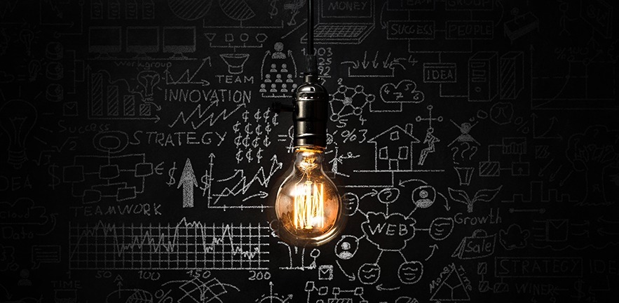 A lightbulb in frotnt of a blackboard of calculations.