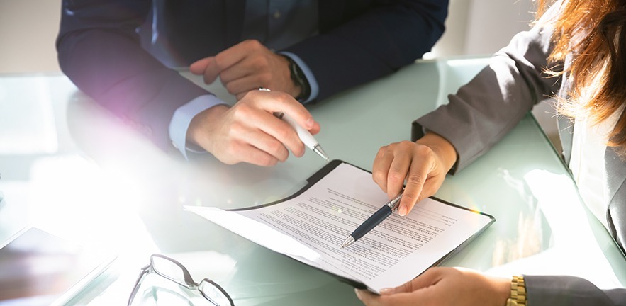 Two businesspeople hand analysing legal document over glass desk.