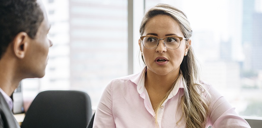 Two business people sitting in office having conversation, woman looking towards man with concerned expression.