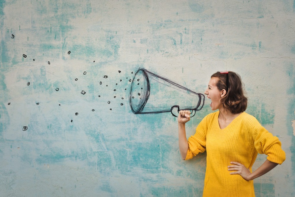 Young woman holding an imaginary megaphone and shouting into it