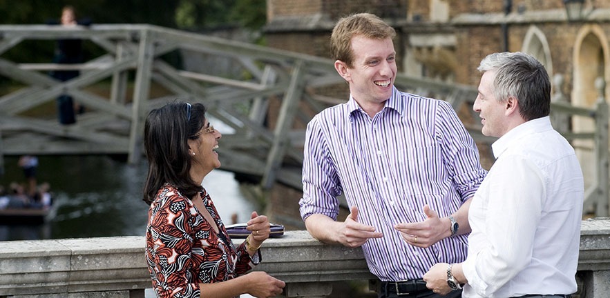 Three Executive MBAs chat with the Mathematical Bridge in the background.