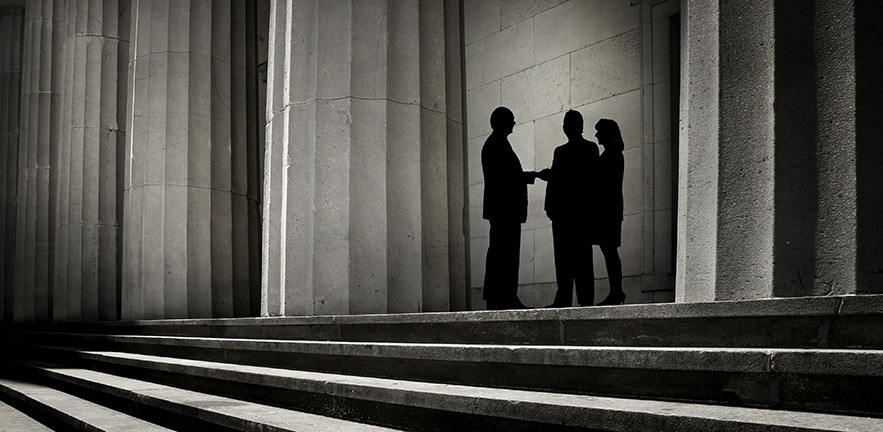 Three people, silhouetted against a backdrop of power, shaking hands.