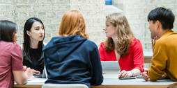 A group of students sit around a table discussing an assignment.