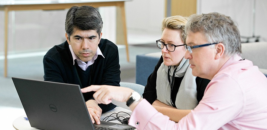 A delegate points to his laptop screen to demonstrate something to his teammates.