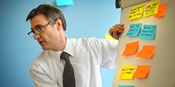 Professor Daniel Ralph at a whiteboard covered in postit notes, leading the class.