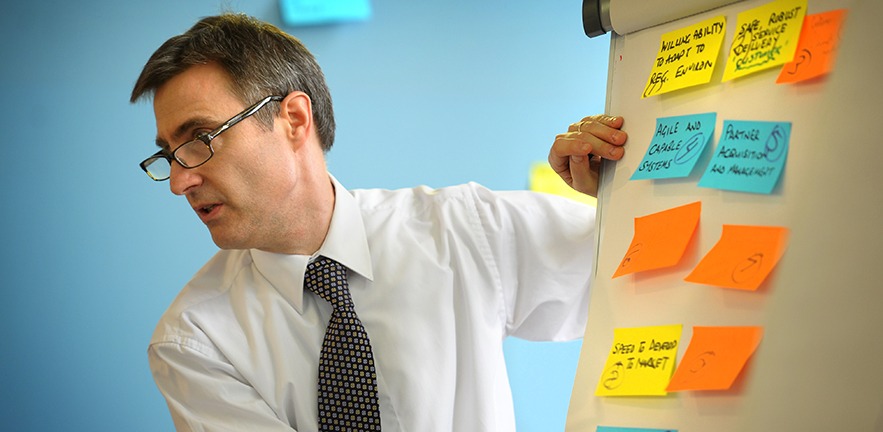 Professor Daniel Ralph at a whiteboard covered in postit notes, leading the class.