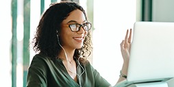 Woman waving at the screen while during a webinar.