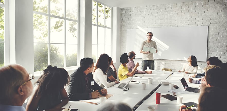 A row of people listening to a woman making a presentation.