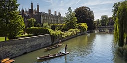 A punt moves past a College on the river Cam on a sunny day.
