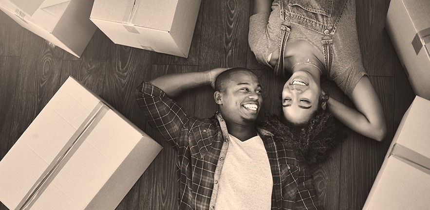 A couple who have just moved into their new home, smiling, surrounded by boxes.