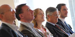 A group of senior executives sit and listen to MBA students presenting their project findings.