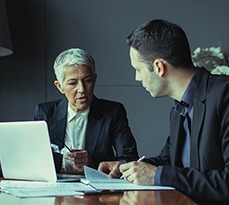 A businesswoman at a laptop discusses something with her assistant.