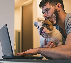 Man sitting at a laptop with a French Bulldog sitting on his lap.