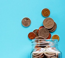 A jar of money with money spilling out onto a bright blue background.