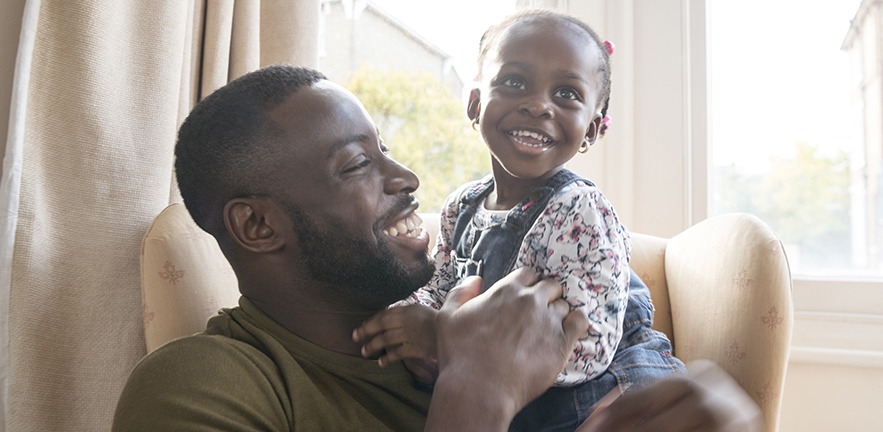 Father with toddler daughter sitting on his lap, both smiling.