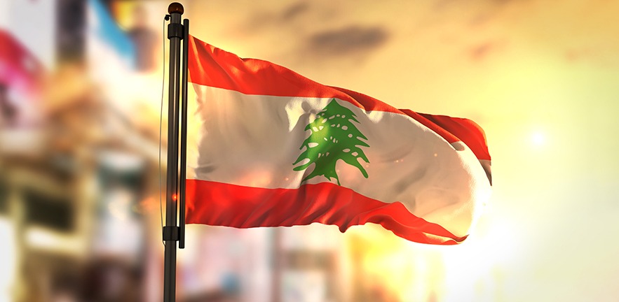 Lebanon Flag Against City Blurred Background At Sunrise Backlight.