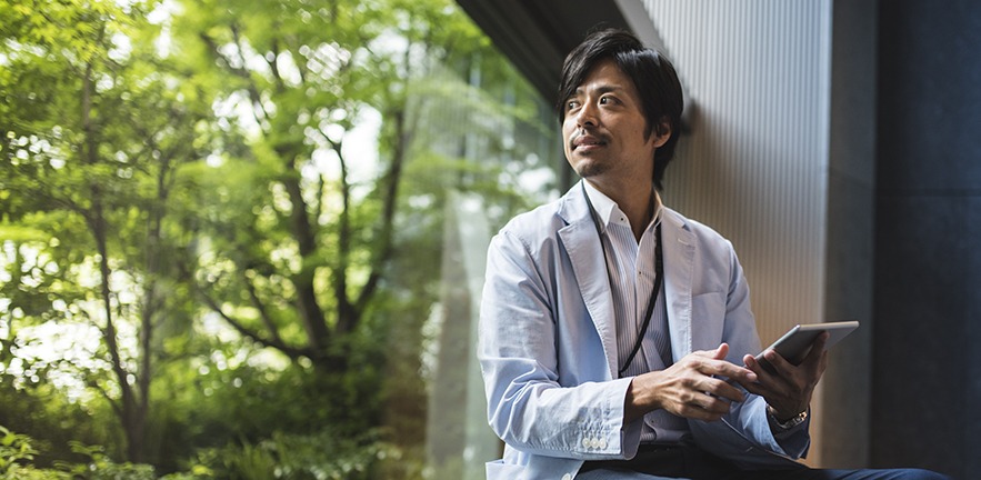 An entrepreneur gazes through the window at a view full of greenery.