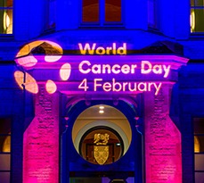 Front facade of Cambridge Judge Business School lit up with colourful lights showing the words World Cancer Day 4 February.